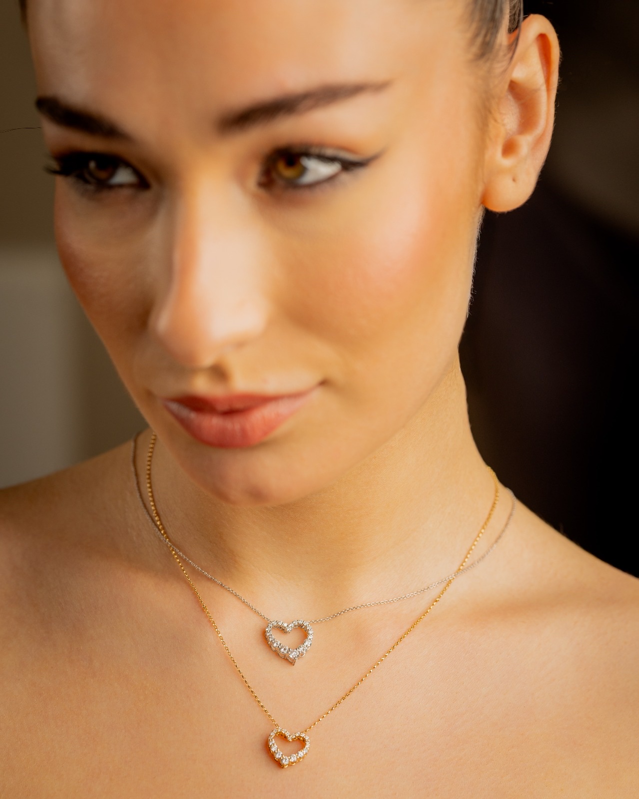 Two diamond-set heart pendants on white and yellow gold chains, worn